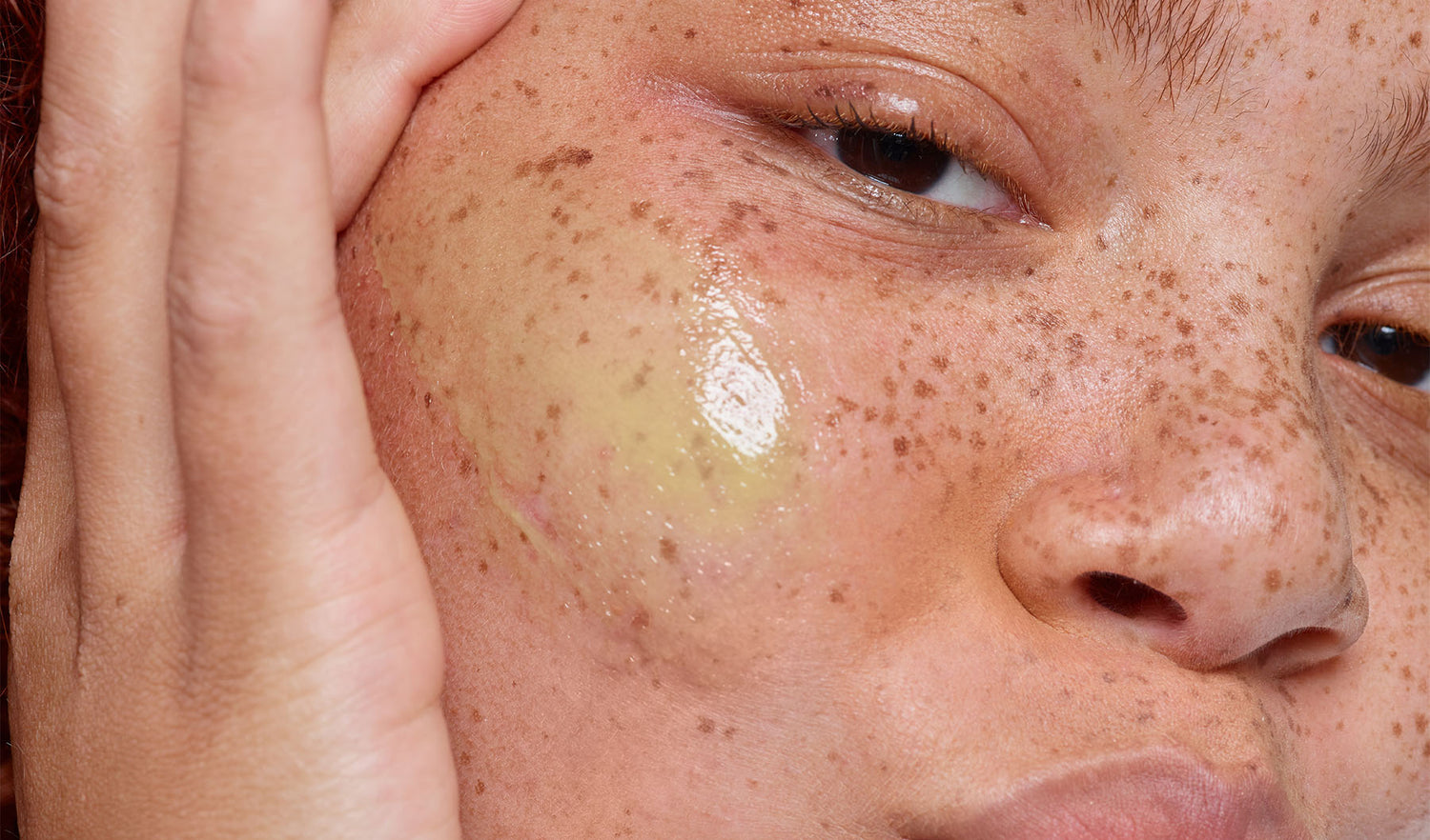 Freckled young woman with a stripe of skincare product on her cheek