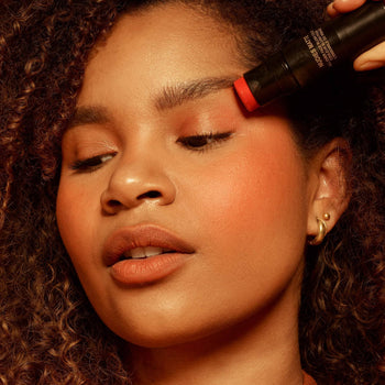 Dark skinned young woman applying Nudies Blush in her eyelid