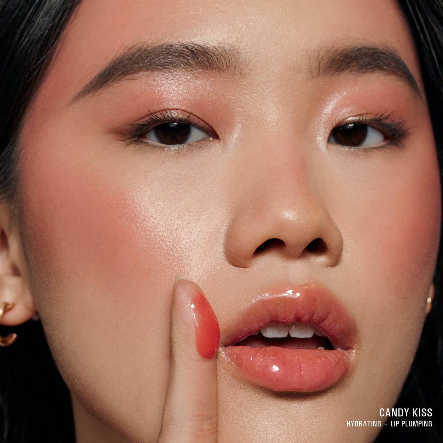 Young woman wearing Hydra-Peptide Lip Butter in shade Candy Kiss with texture swatch on her finger