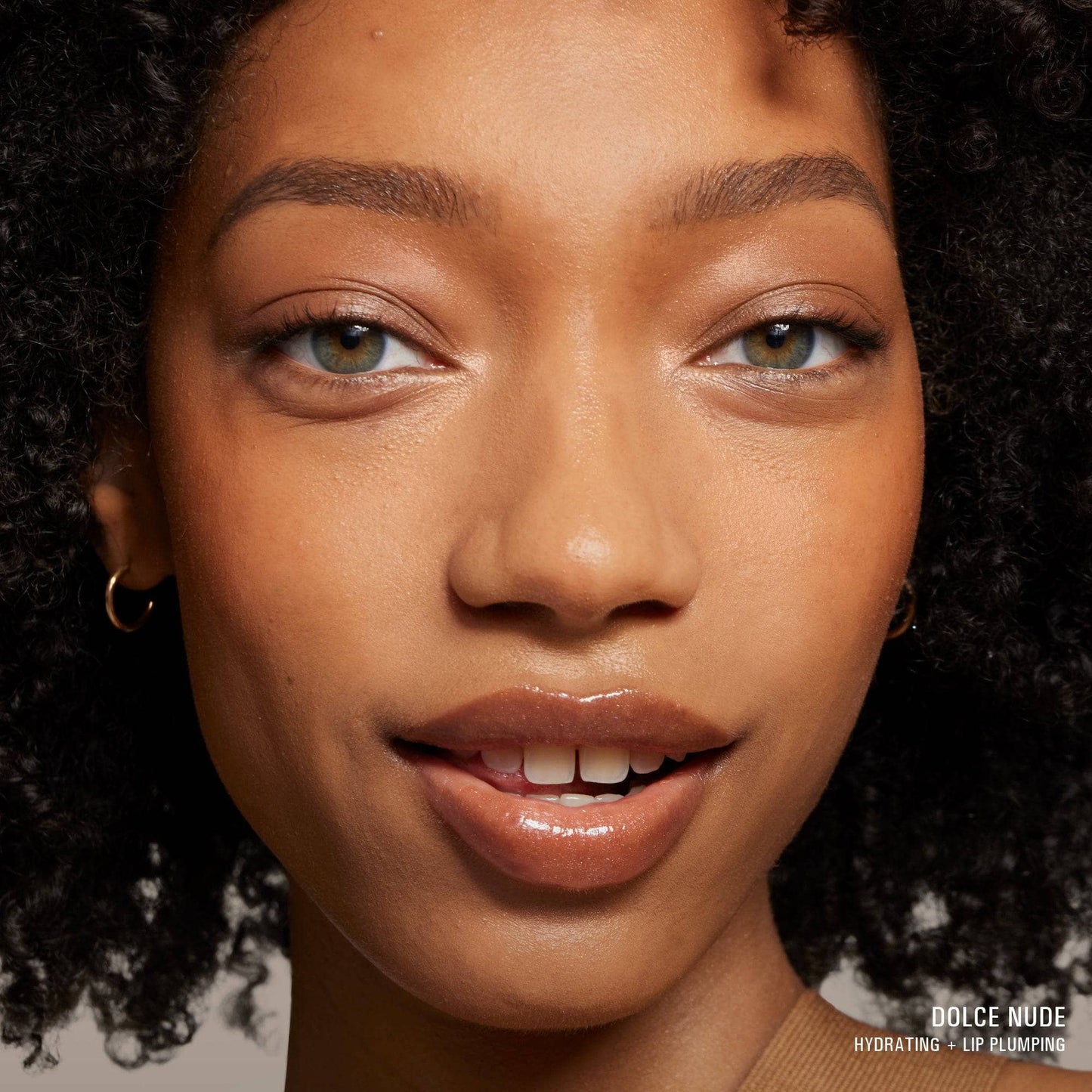 Dark skinned young woman with green eyes wearing Hydra-Peptide Lip Butter in shade Dolce Nude