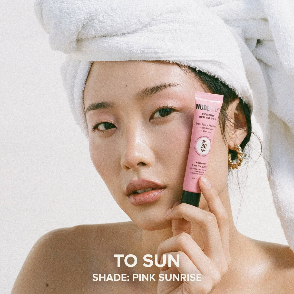 Model holding a tube of Nudescreen blush tint in shade PINK SUNRISE