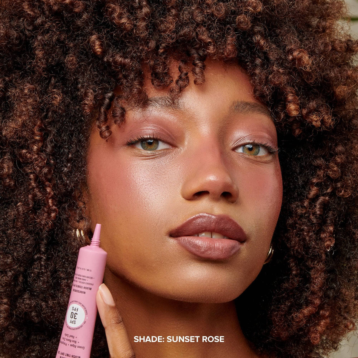 Dark skinned young woman applying Nudescreen Blush Tint Sunset Rose on her cheeks - 11