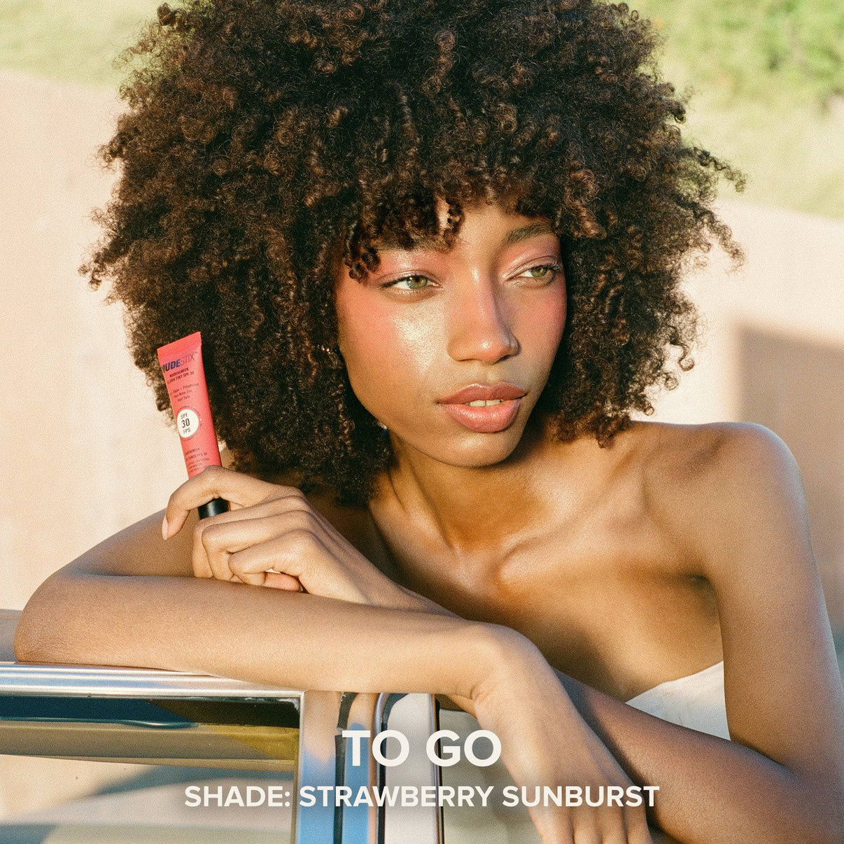 Model holding a tube of Nudescreen blush tint in shade STRAWBERRY SUNBURST