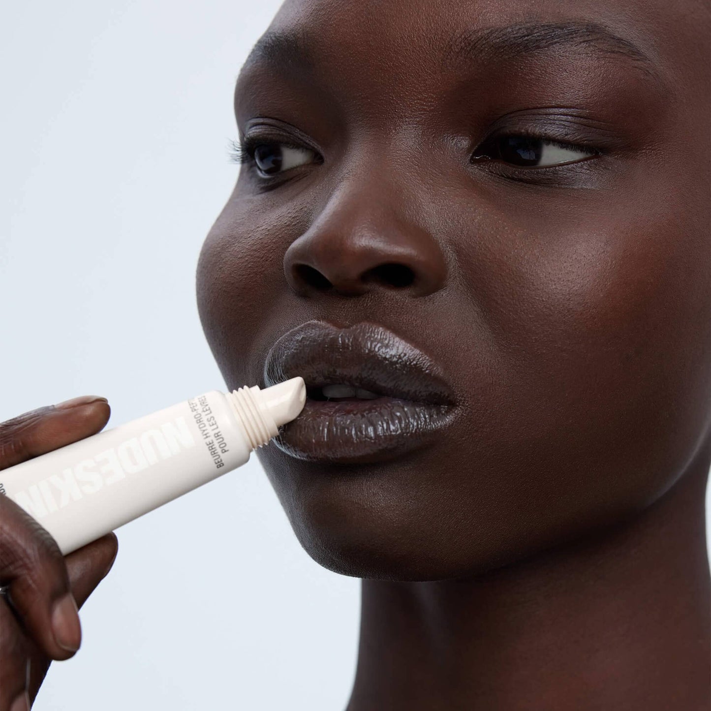 Dark skinned young woman applying on Hydra-Peptide Lip Butter in shade Clear Gloss