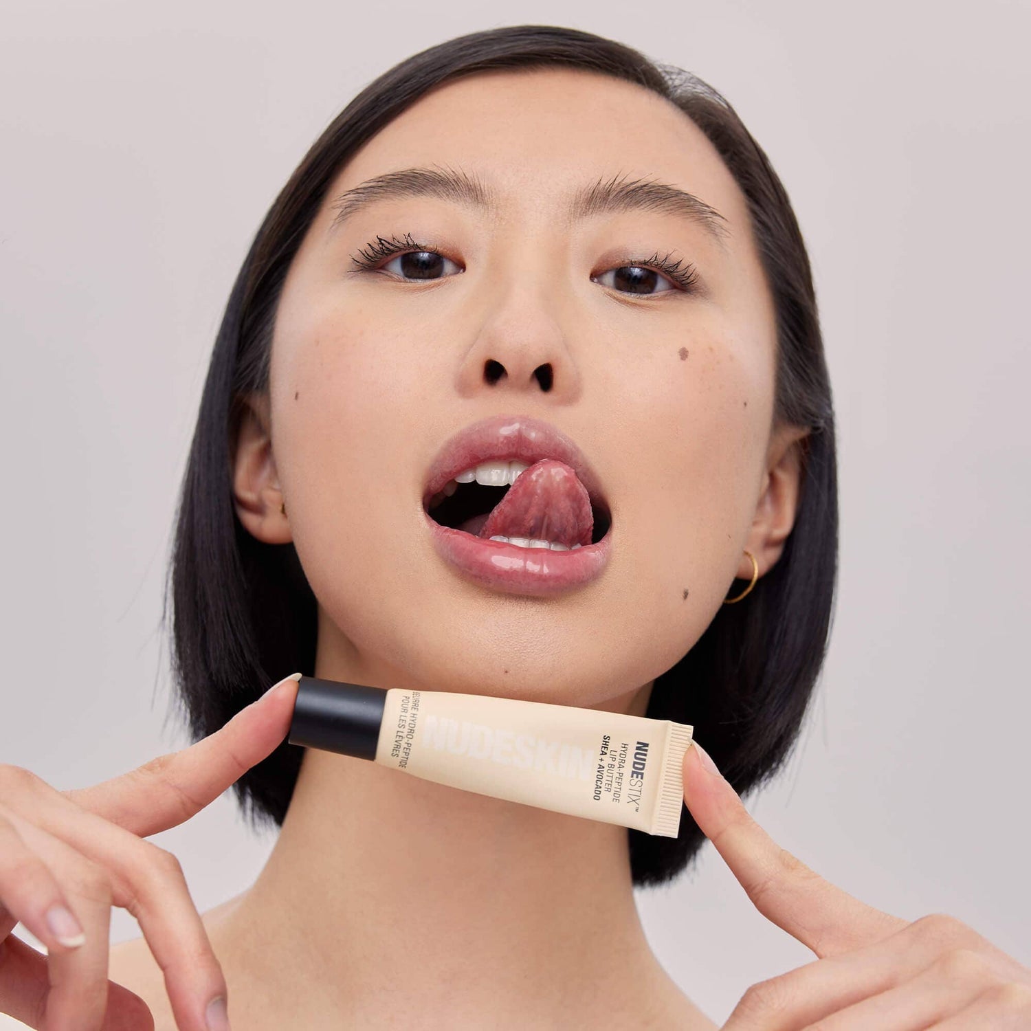 Asian young woman holding a tube of Hydra-Peptide Lip Butter Clear Gloss