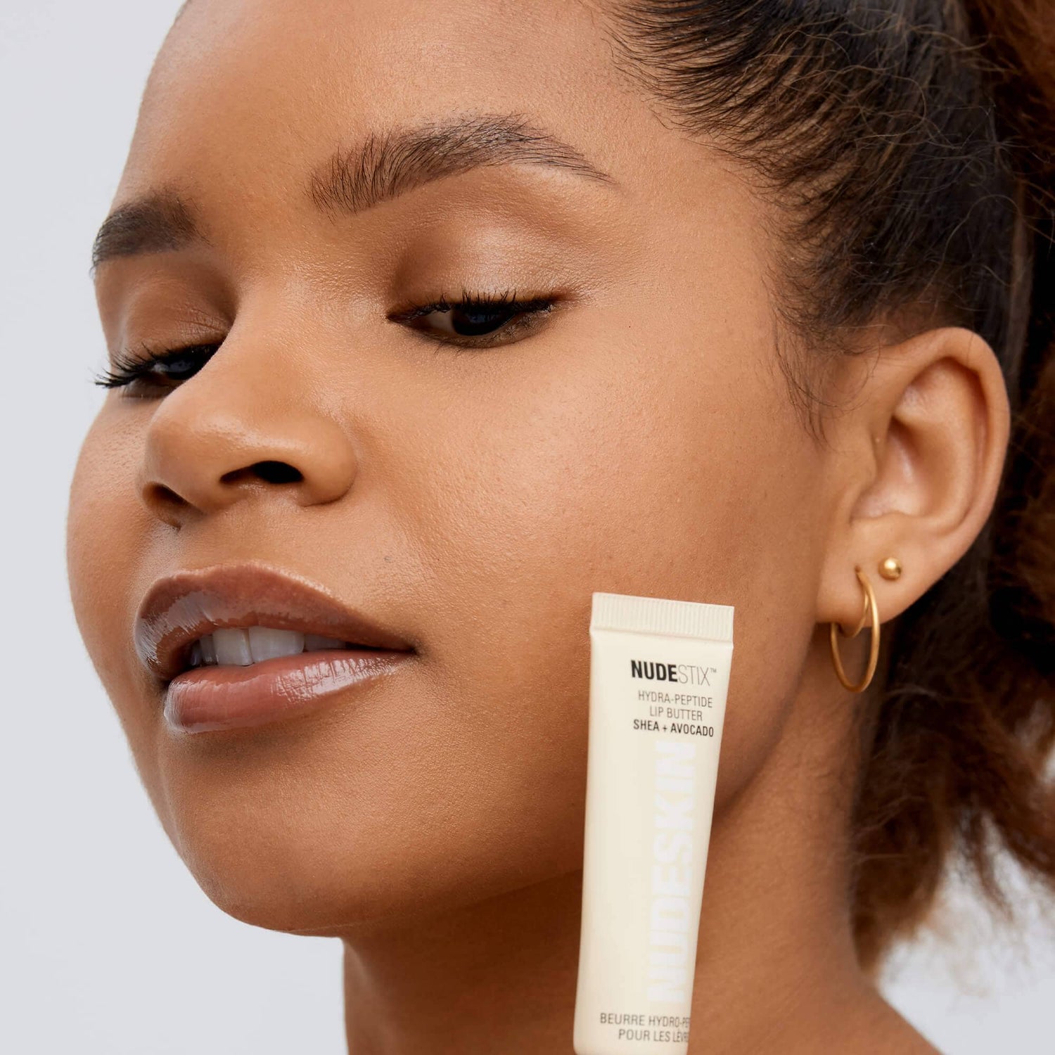 Mixed race young woman holding a tube of Hydra-Peptide Lip Butter Clear Gloss
