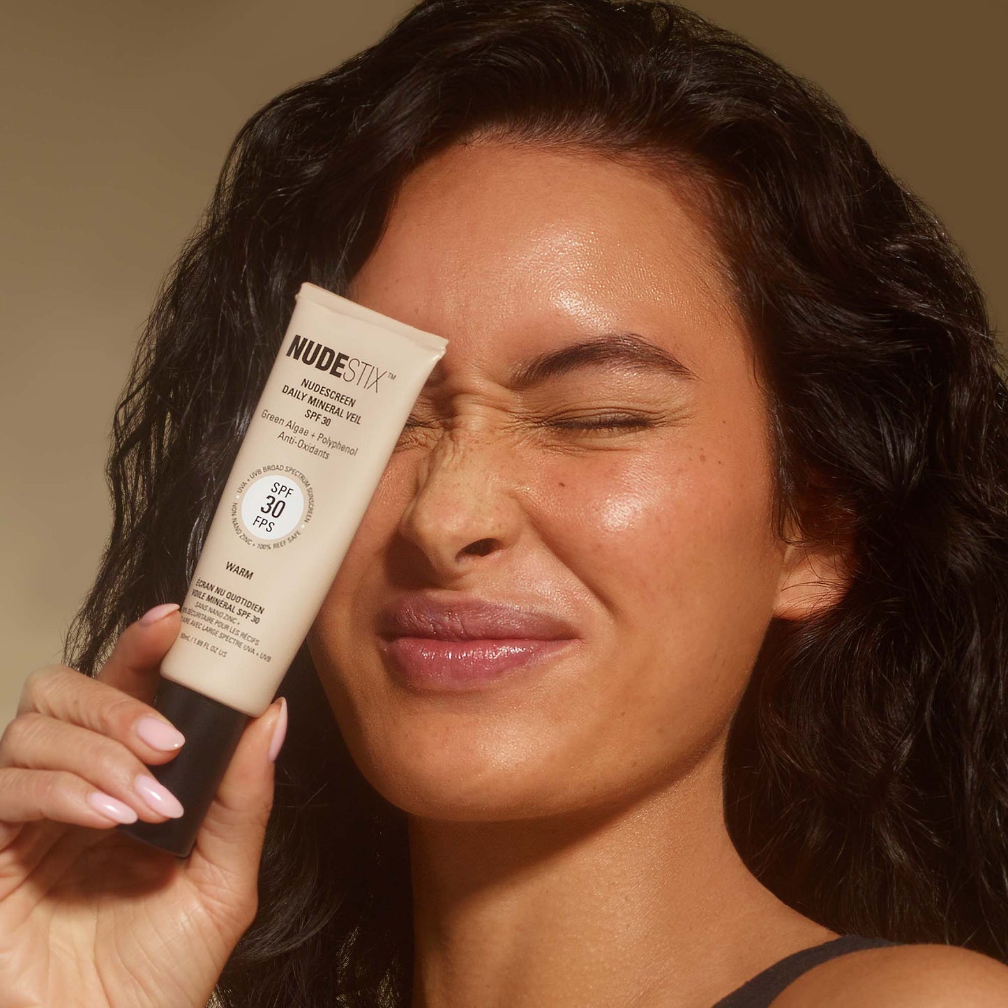 Young woman holding a tube of Nudescreen SPF Moisturizer in shade Warm