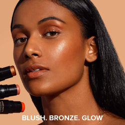 Dark skinned young woman holding three Nudies Glow Highlighter Sticks in different shades