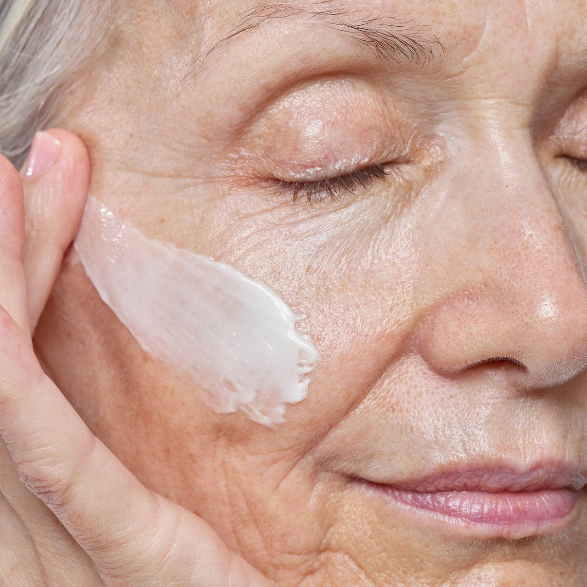 Mature woman applying Citrus-C Mask & Daily Moisturizer on her cheek