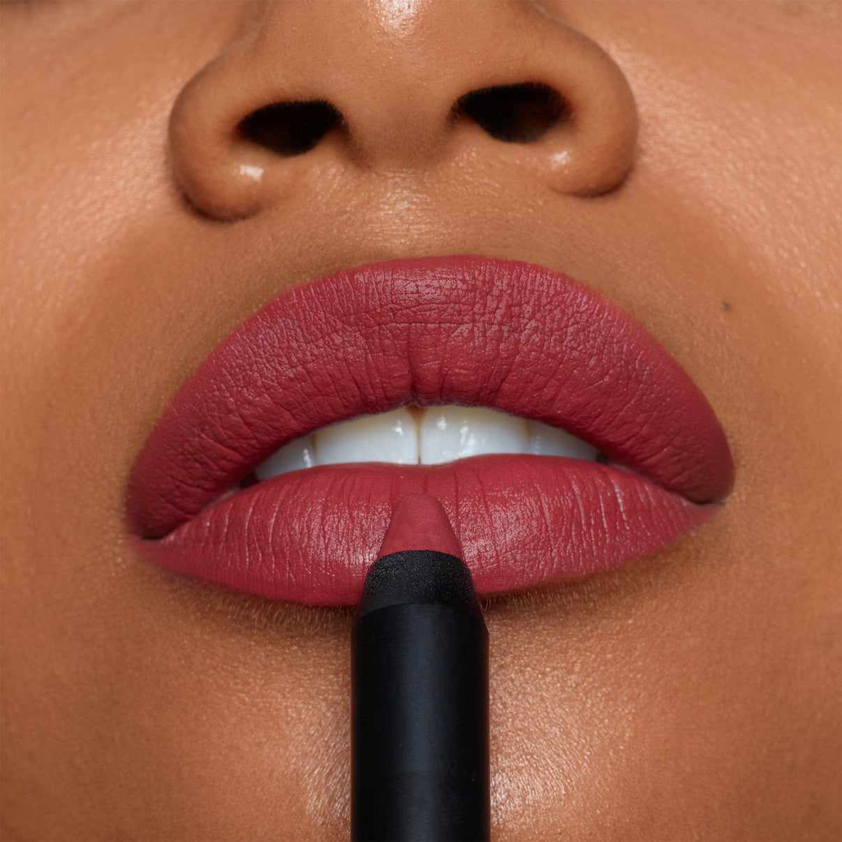 Dark skinned woman applying on Intense Matte Lip + Cheek pencil in shade retro